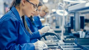 Female Electronics Factory Workers in Blue Work Coats and Protective Glasses Assemble Printed Circuit Boards