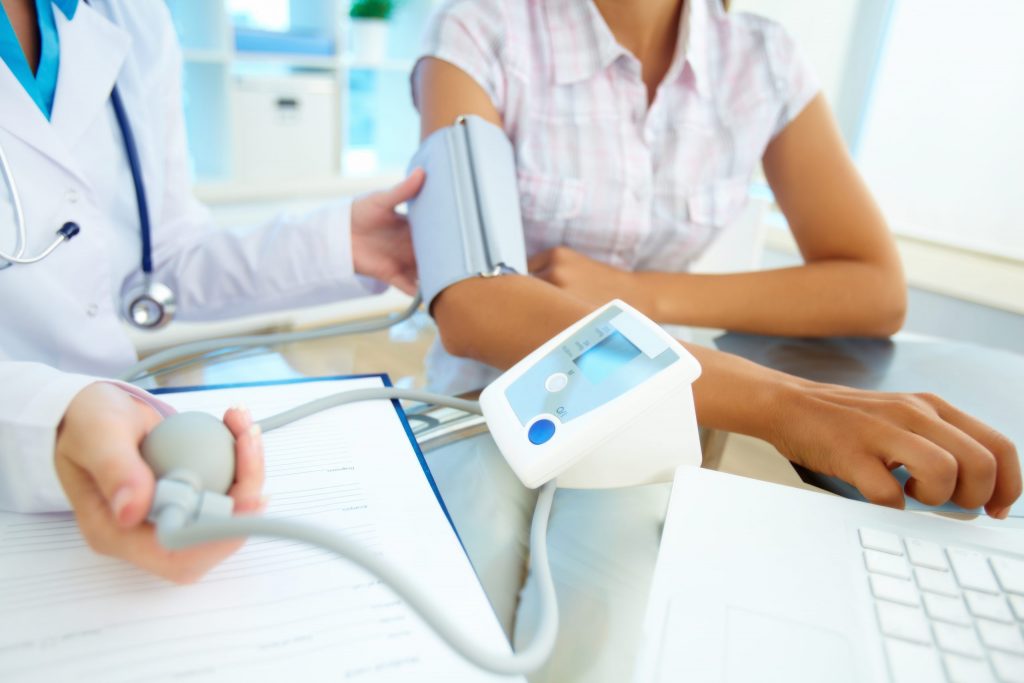 Close-up of a doctor using an automatic blood pressure cuff on a patient in a brightly lit office